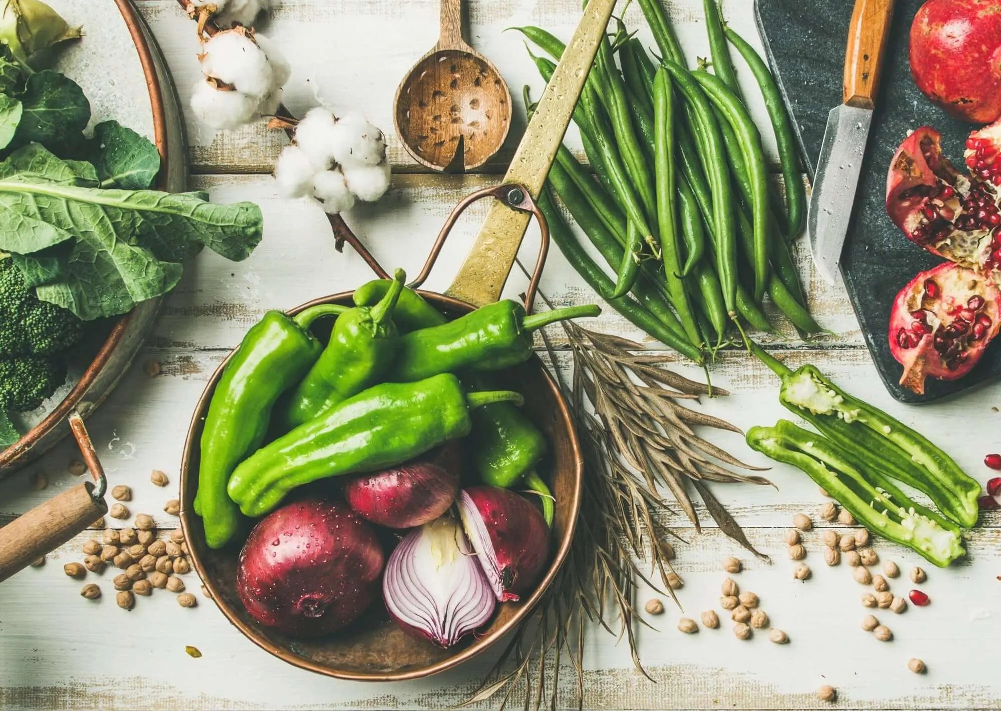 Texto alternativo:Ingredientes frescos para alimentação vegetariana e vegana, incluindo pimentões, cebolas, vagens e romãs.