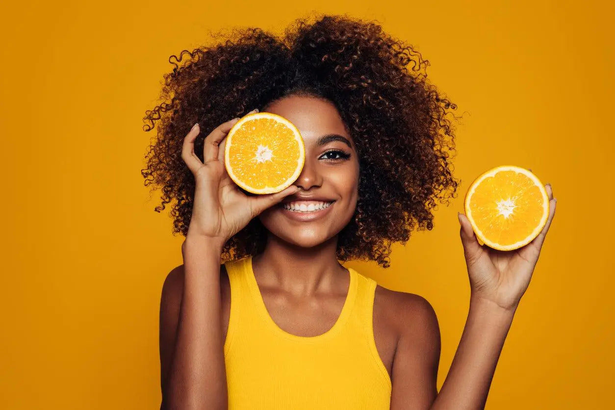 Mulher sorridente segurando laranjas, símbolo de vitamina C e imunidade.