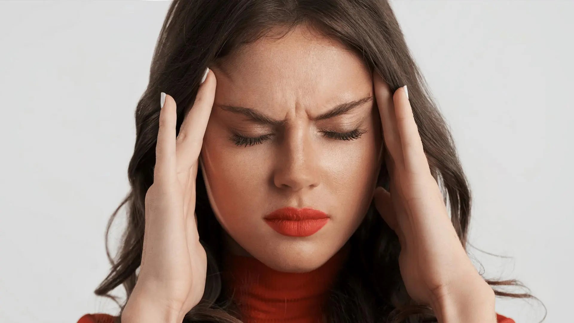Texto alternativo:Mulher com expressão de dor segurando a cabeça, representando enxaqueca.
