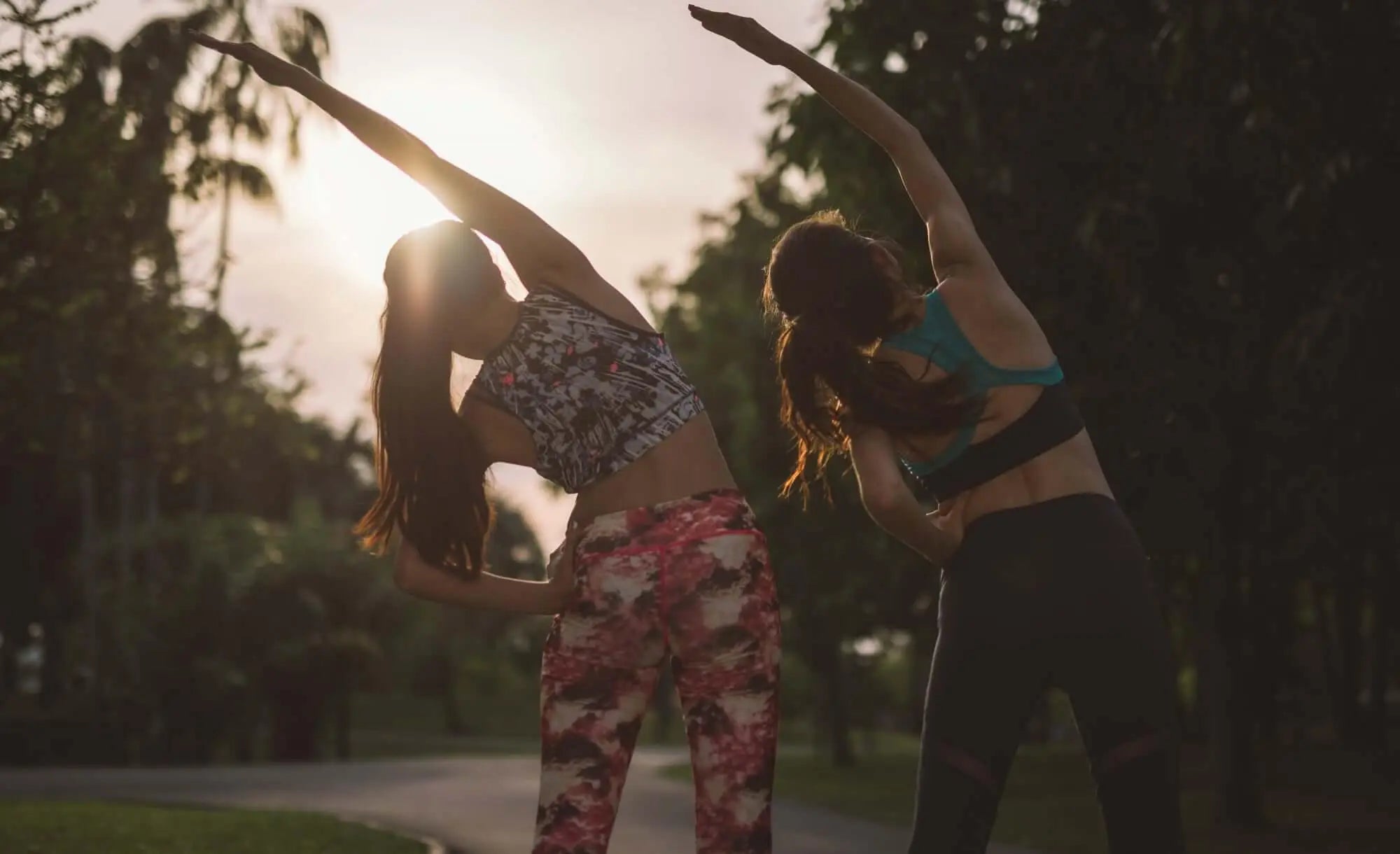 Mulheres praticando exercícios ao ar livre ao pôr do sol, promovendo saúde.
