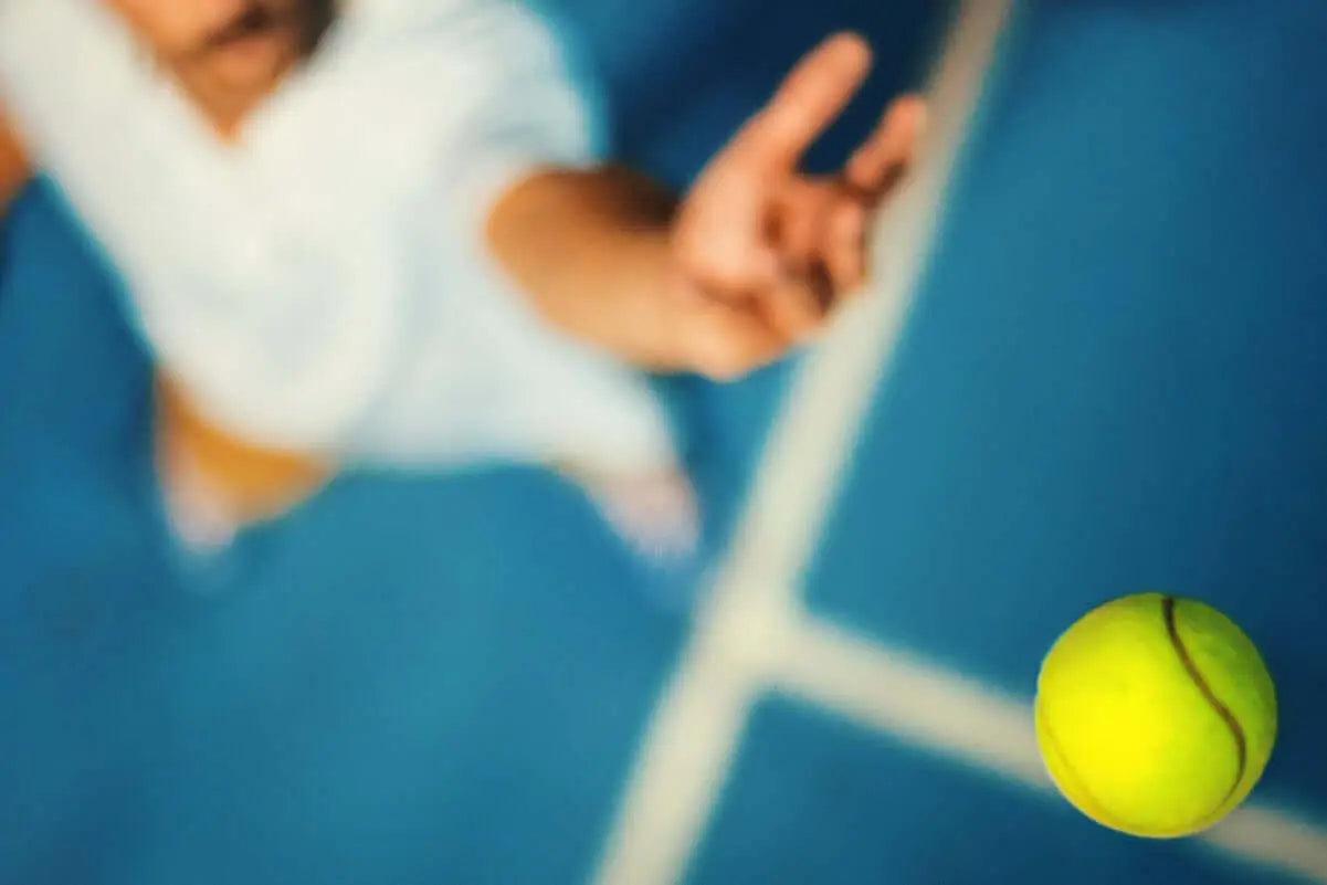 Texto alternativo:Jogador de tênis em ação, lançando a bola em quadra azul.