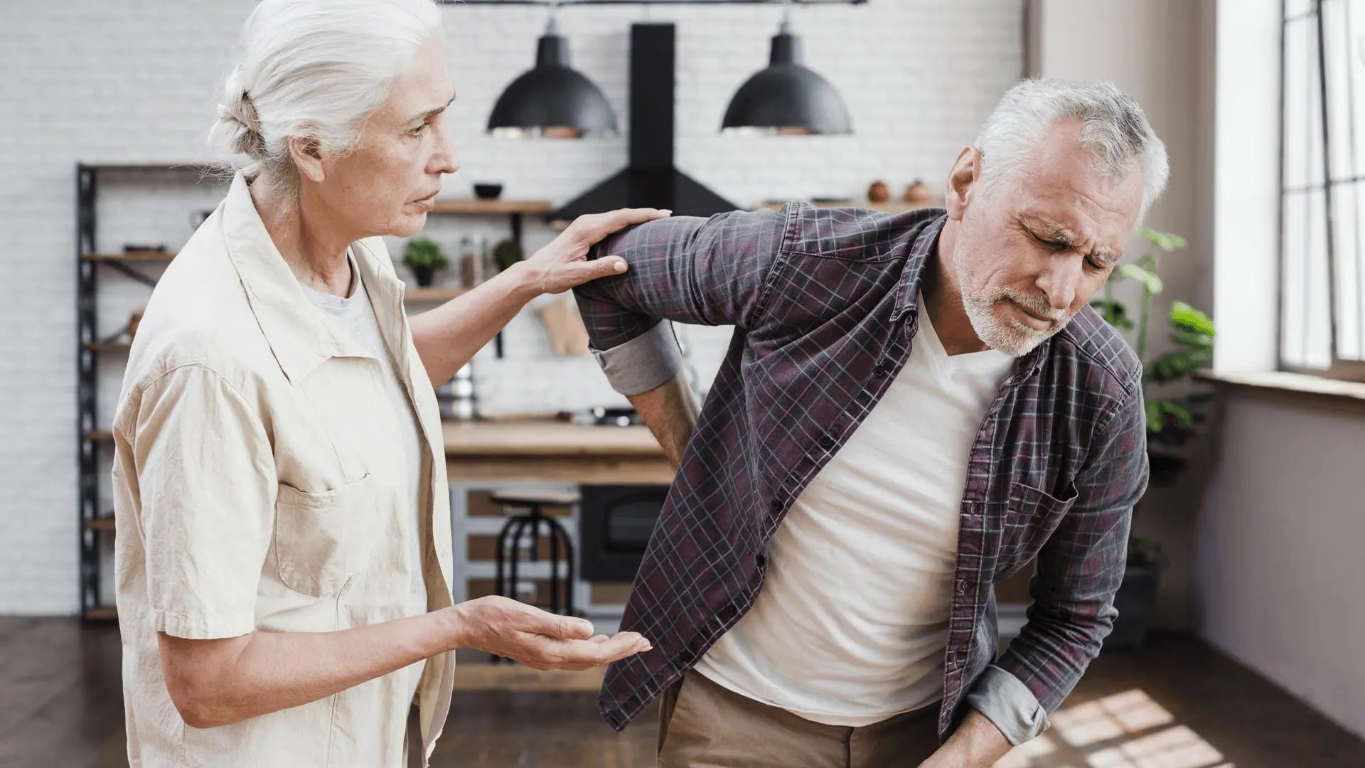 Casal idoso discutindo saúde óssea, homem com dor nas costas em casa.