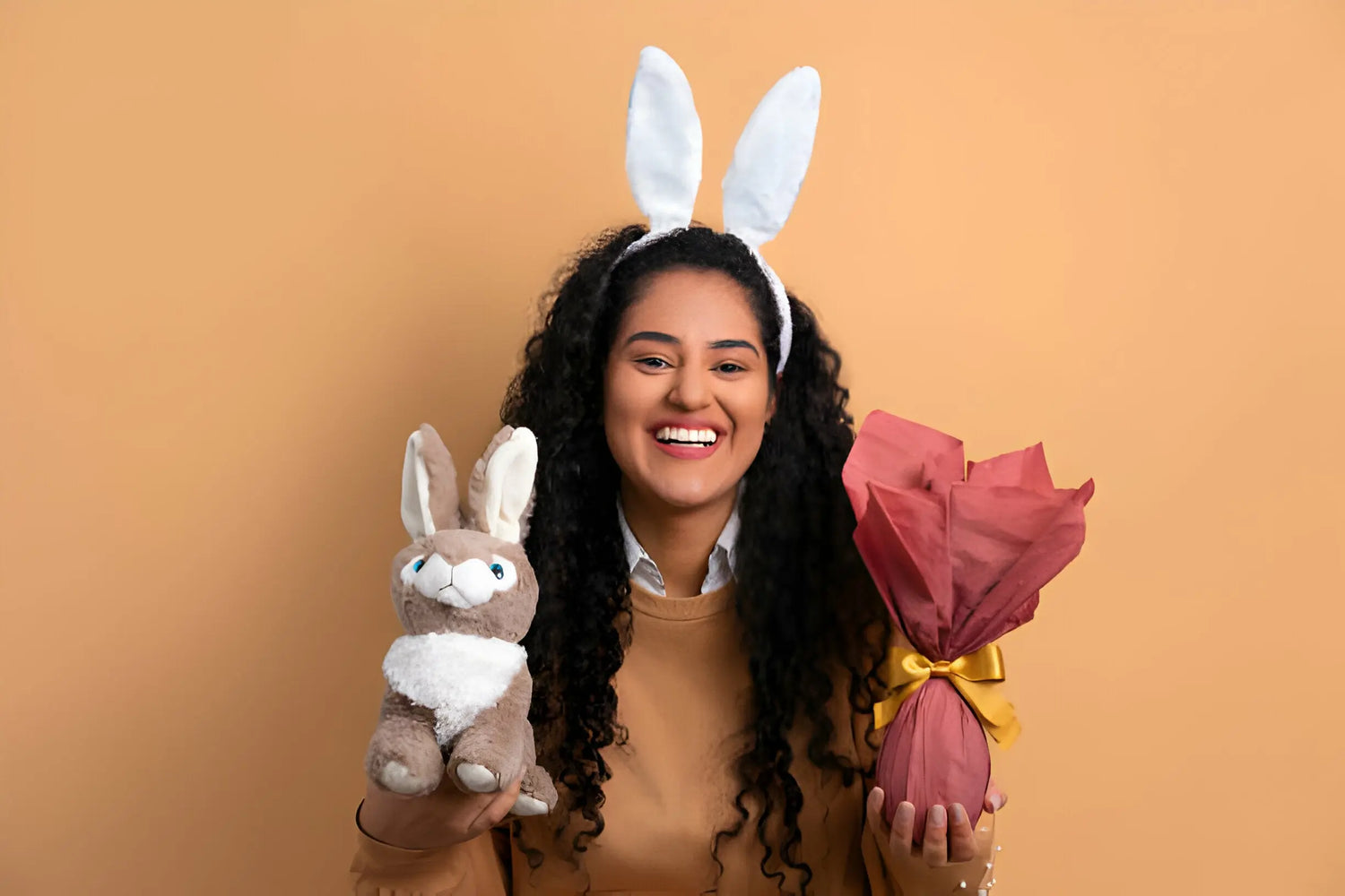 Mulher sorridente com orelhas de coelho segurando ovo de Páscoa e pelúcia.
