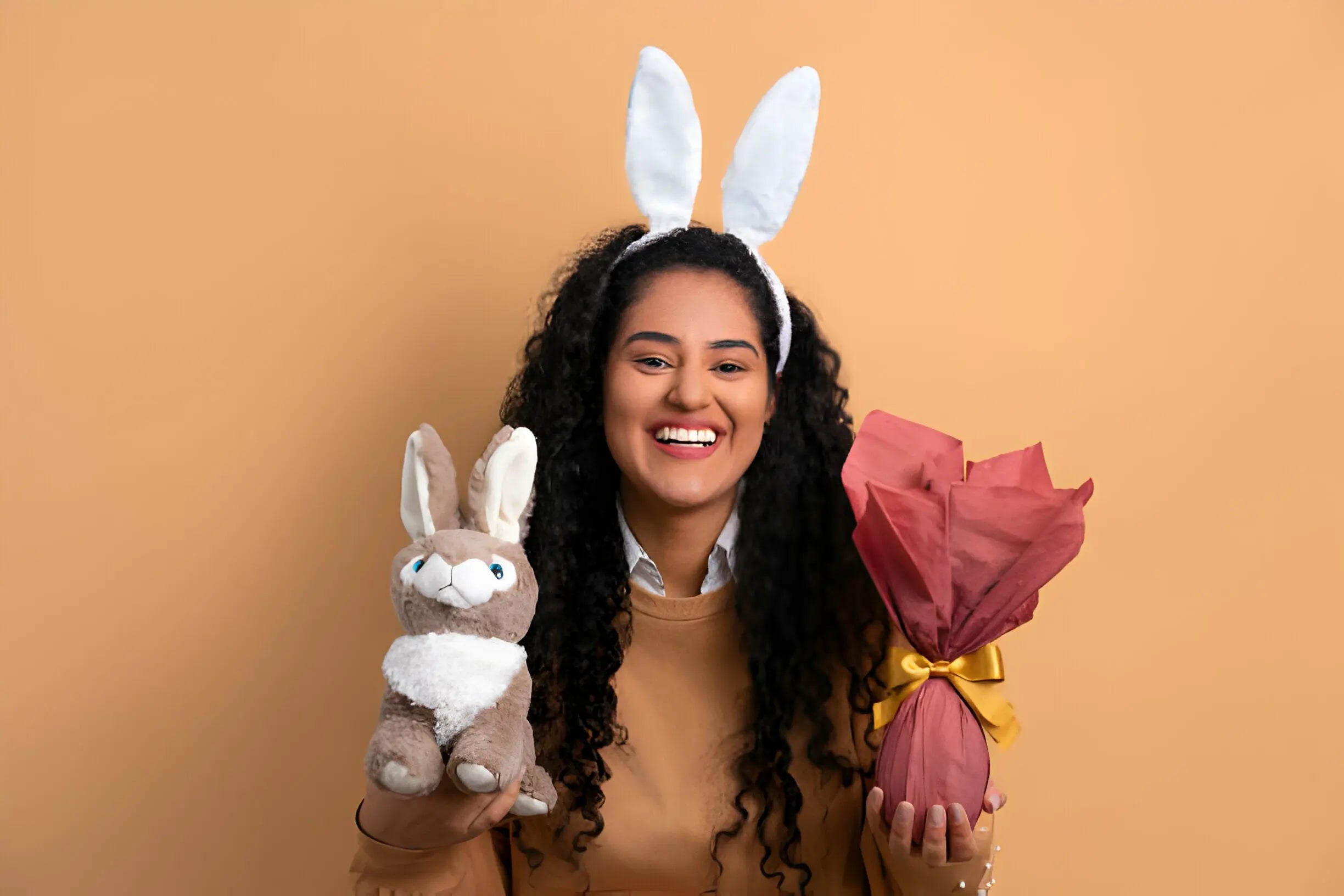 Mulher sorridente com orelhas de coelho segurando ovo de Páscoa e pelúcia.