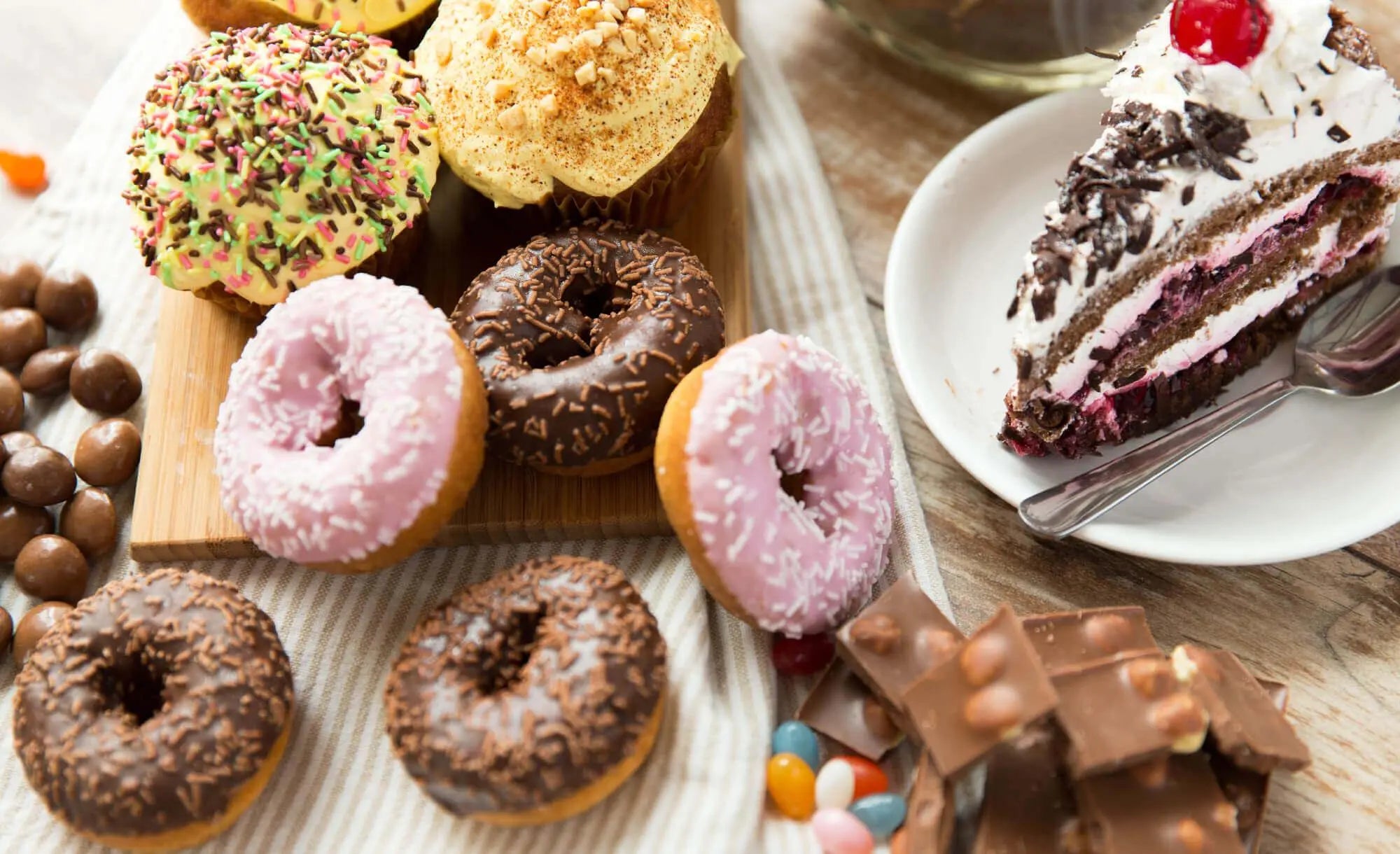 Variedade de doces, incluindo donuts, cupcakes e bolo, em mesa atrativa.