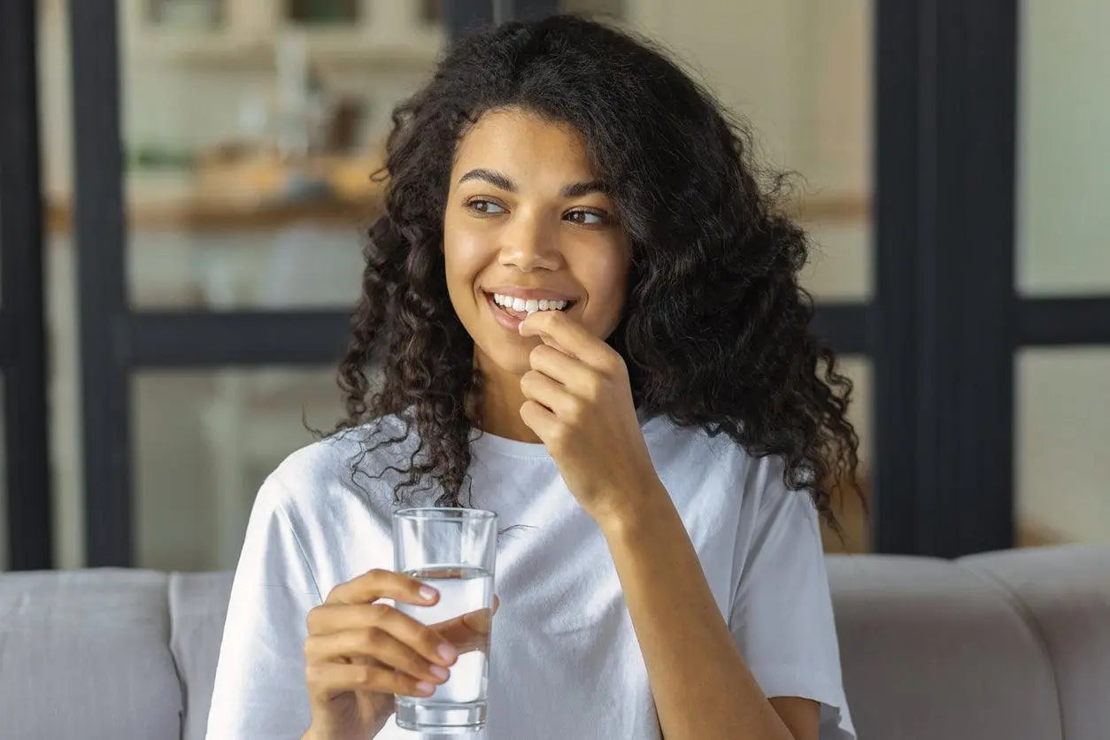 Mulher sorridente segurando um copo de água enquanto toma um suplemento.