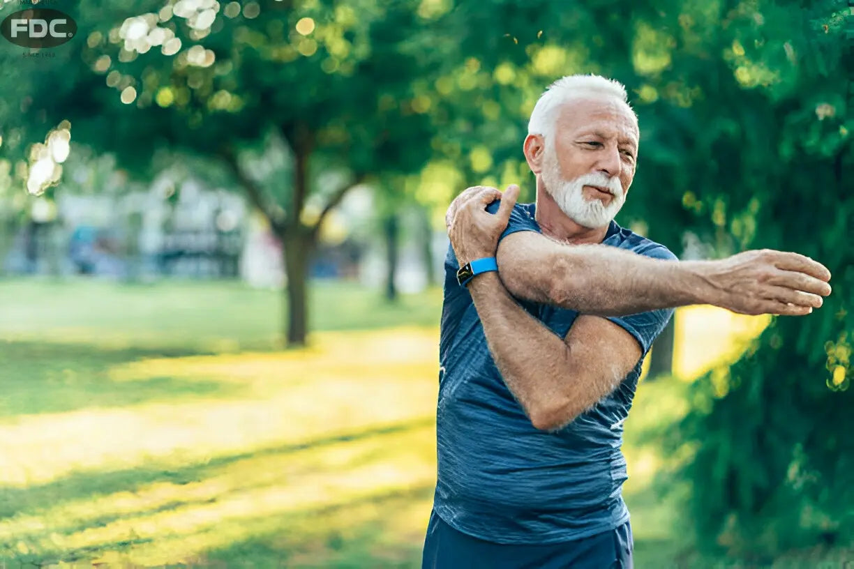 Homem idoso alongando o braço em parque, aliviando dores nas articulações.