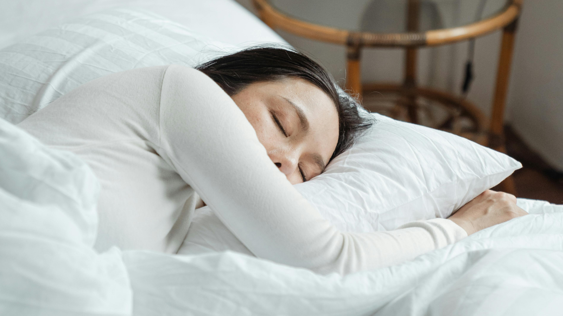 Texto alternativo:Mulher dormindo tranquilamente em cama branca, simbolizando sono melhorado.