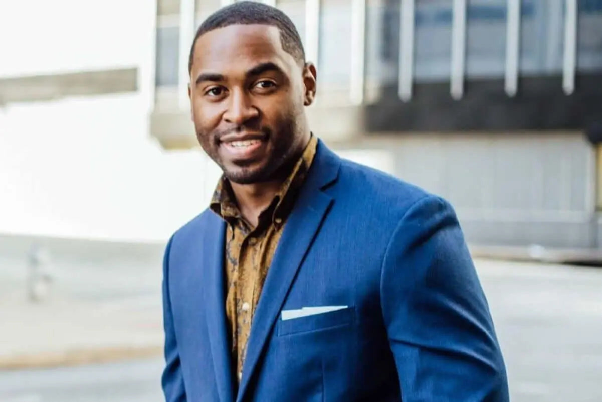 Homem sorridente vestindo terno azul em ambiente urbano.