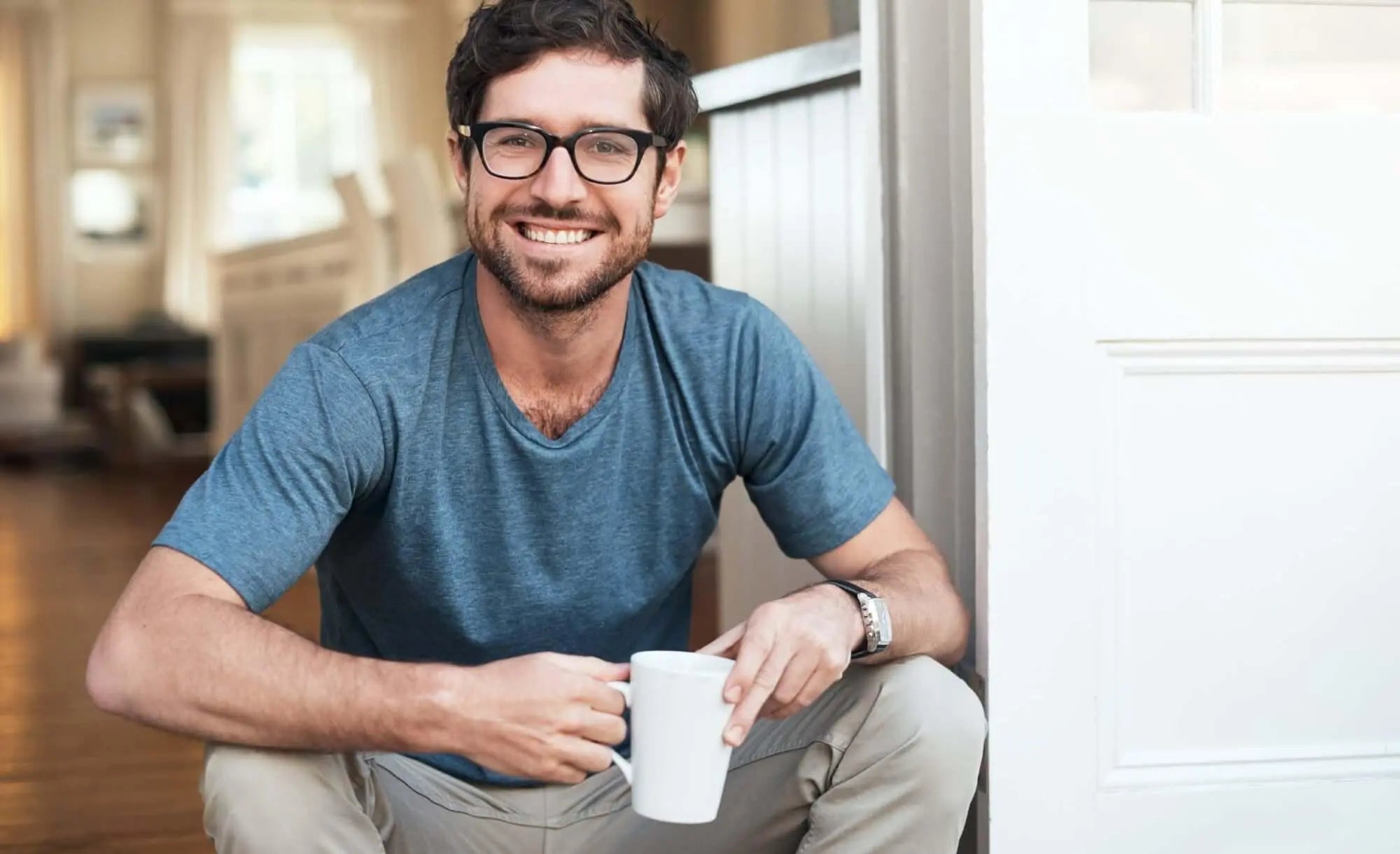 Homem sorridente com óculos segurando uma xícara, simbolizando bem-estar e saúde.