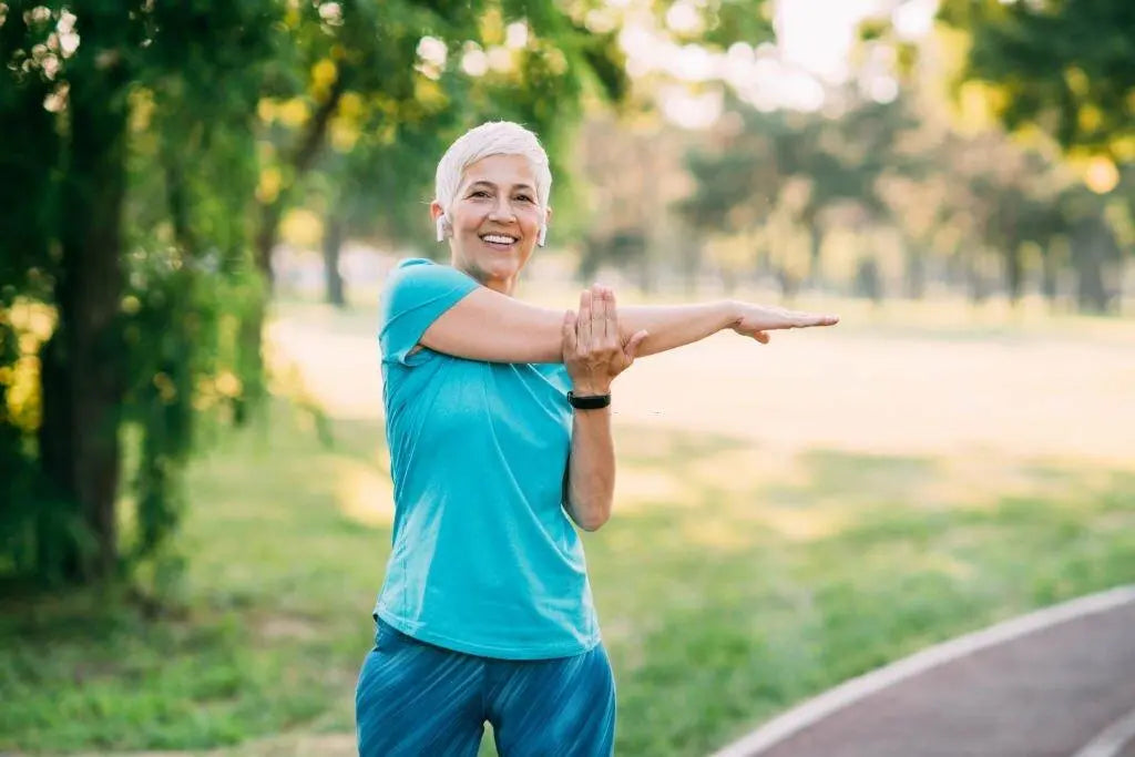 Mulher madura praticando alongamento ao ar livre, promovendo saúde óssea.