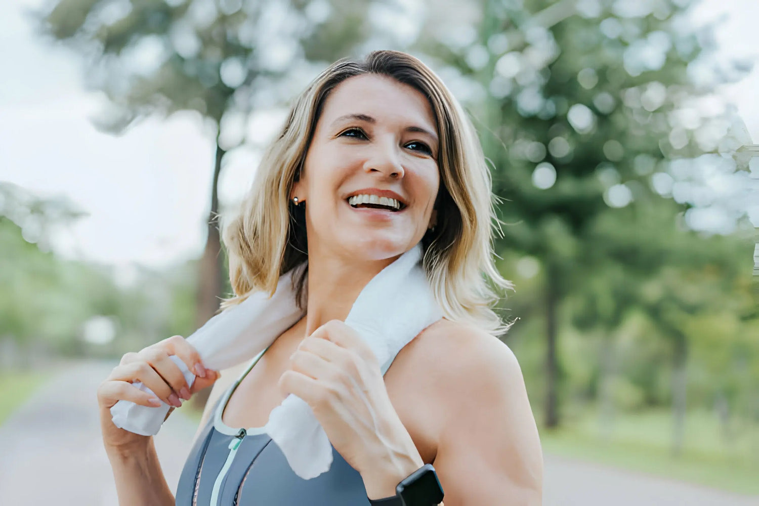 Mulher sorridente com toalha no pescoço após exercício ao ar livre.