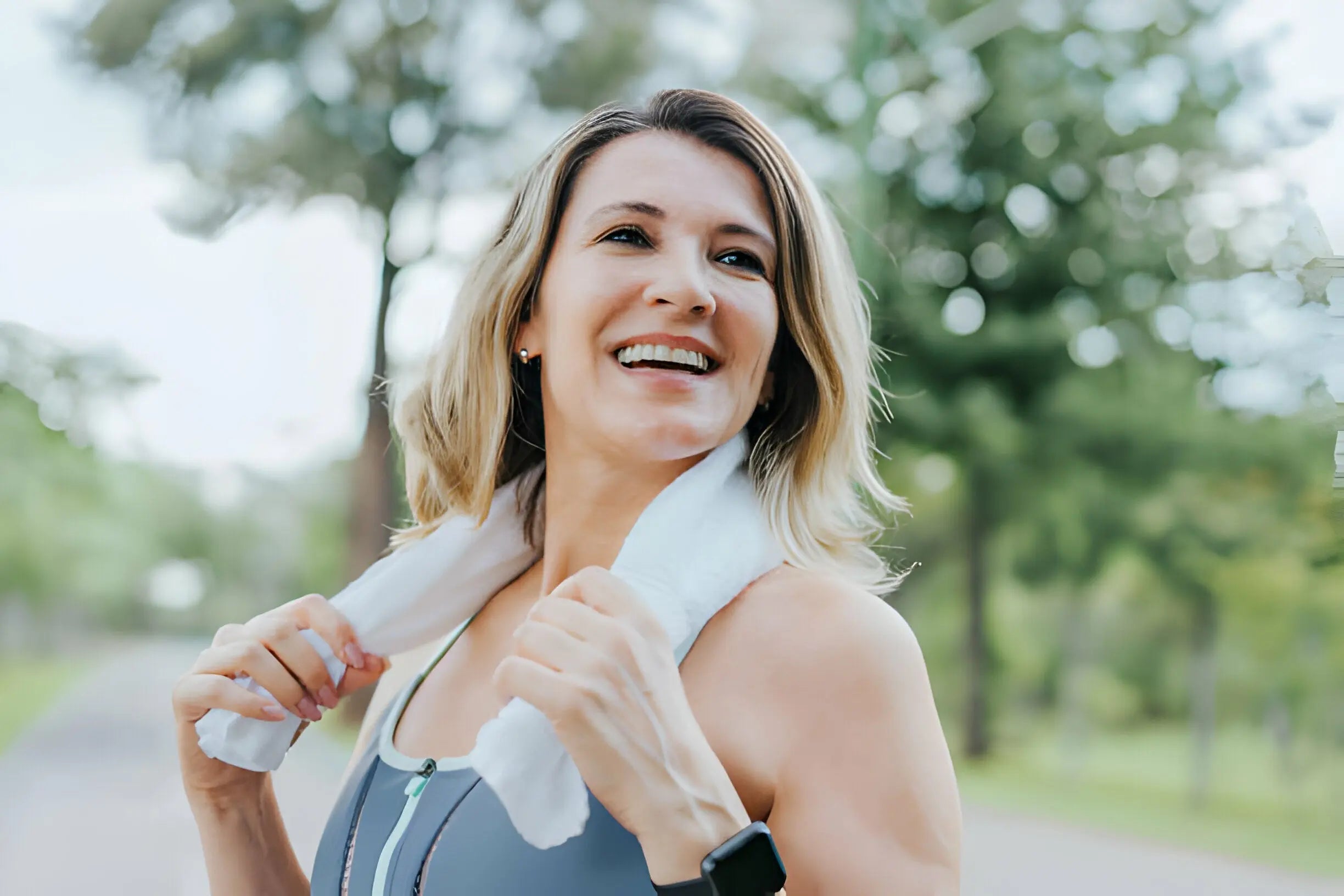 Mulher sorridente com toalha no pescoço após exercício ao ar livre.
