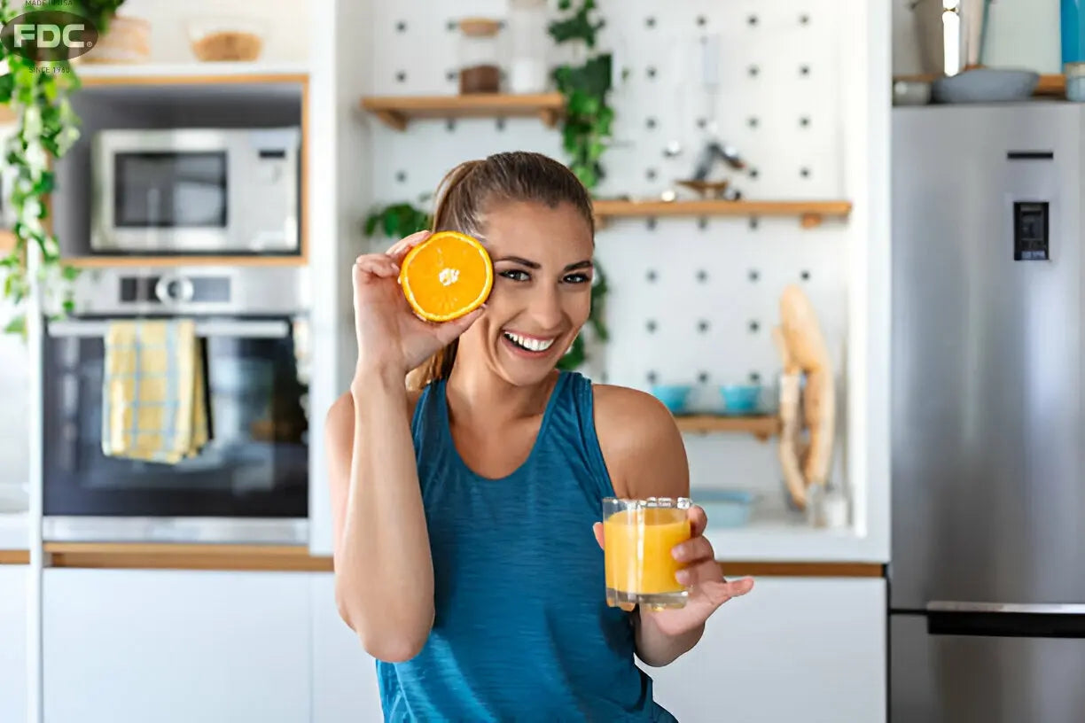 Texto alternativo:Mulher sorridente segurando suco de laranja e metade de uma laranja, destacando a vitamina C para imunidade.