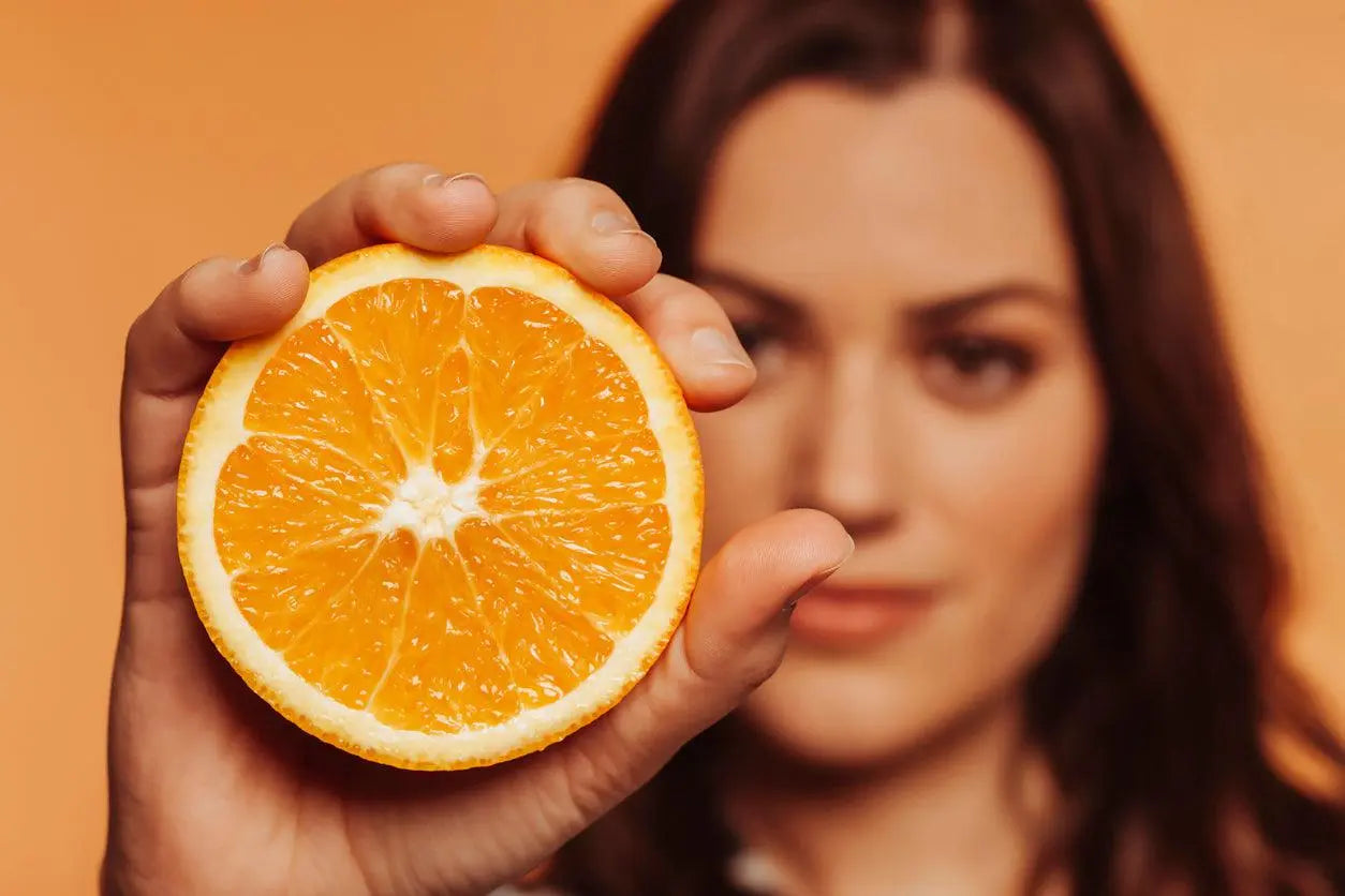 Texto alternativo:Mulher segurando metade de uma laranja, destacando a vitamina C.
