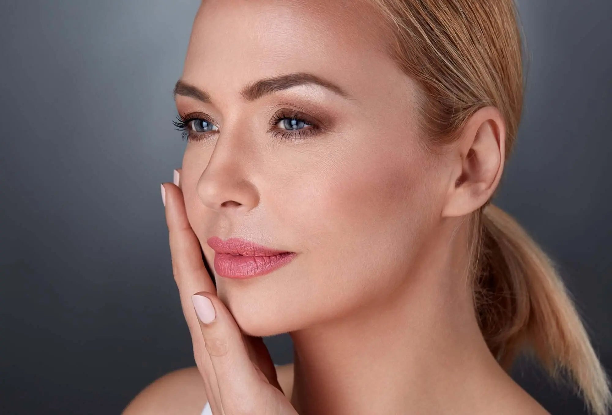 Mulher tocando o rosto com pele saudável, destacando a relação entre vitamina D e pele.