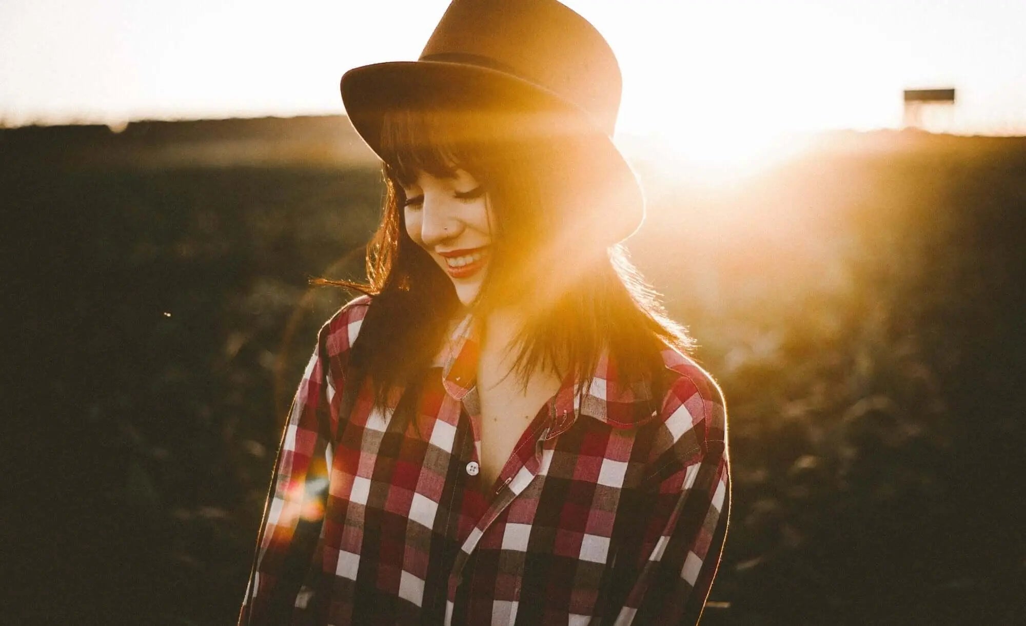 Mulher sorrindo ao pôr do sol, destacando saúde e bem-estar.