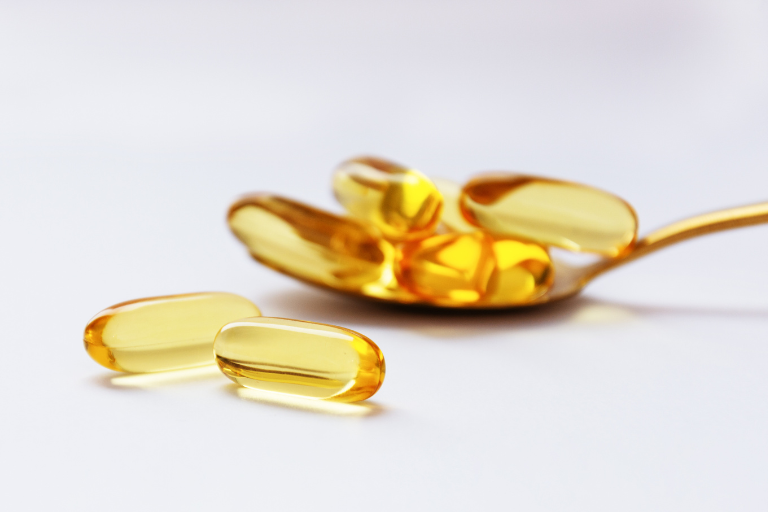 Cápsulas de Ômega-3 douradas em uma colher, destacando sua pureza e qualidade.