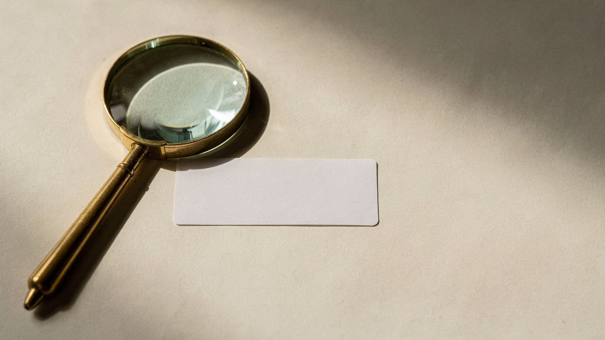Etiqueta de papel em branco sobre superfície creme ao lado de uma lupa de latão