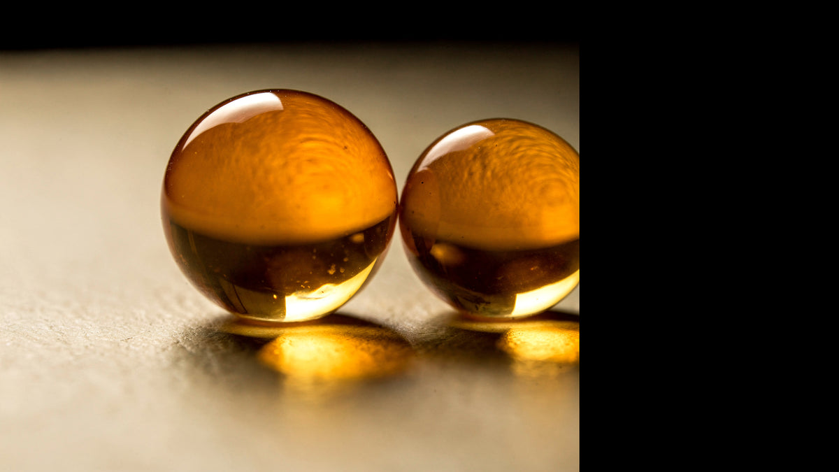 Macro de duas esferas translúcidas douradas lado a lado, iluminadas por trás, sobre superfície creme