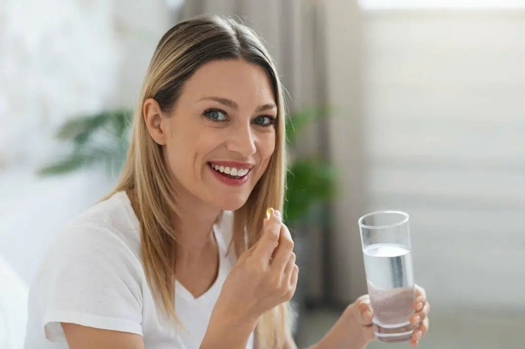 Mulher sorridente tomando cápsula de ômega-3 com um copo de água.