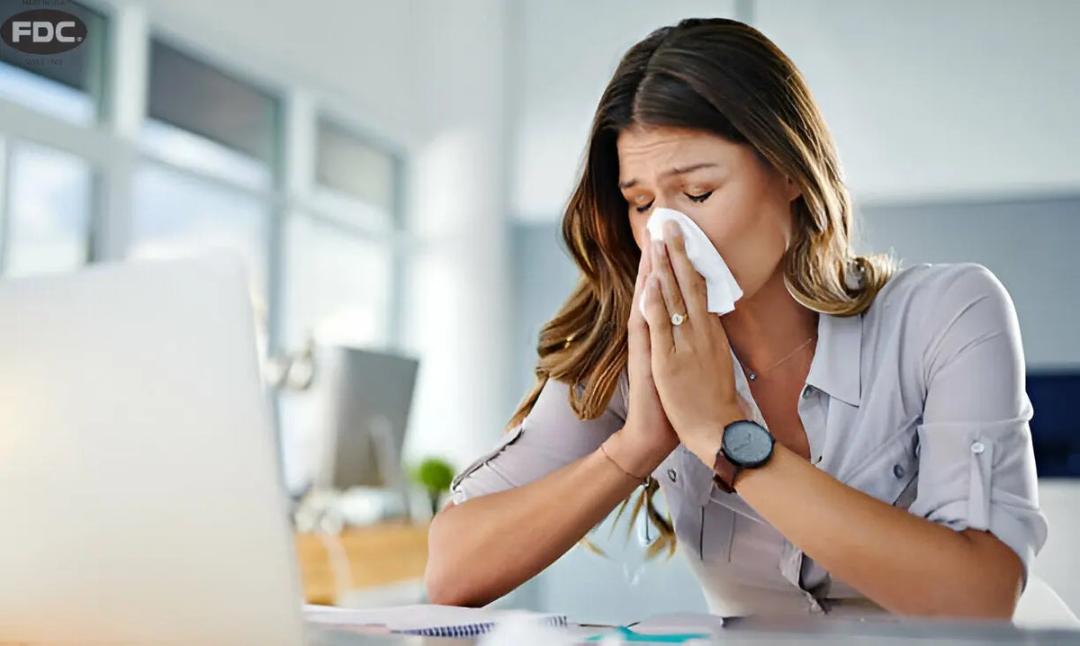 Mulher resfriada no trabalho limpando o nariz com lenço, simbolizando baixa imunidade no inverno.