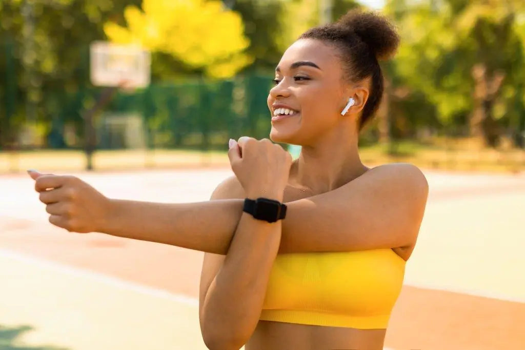 Texto alternativo:Mulher sorridente alongando-se ao ar livre, com fones de ouvido e roupa esportiva.
