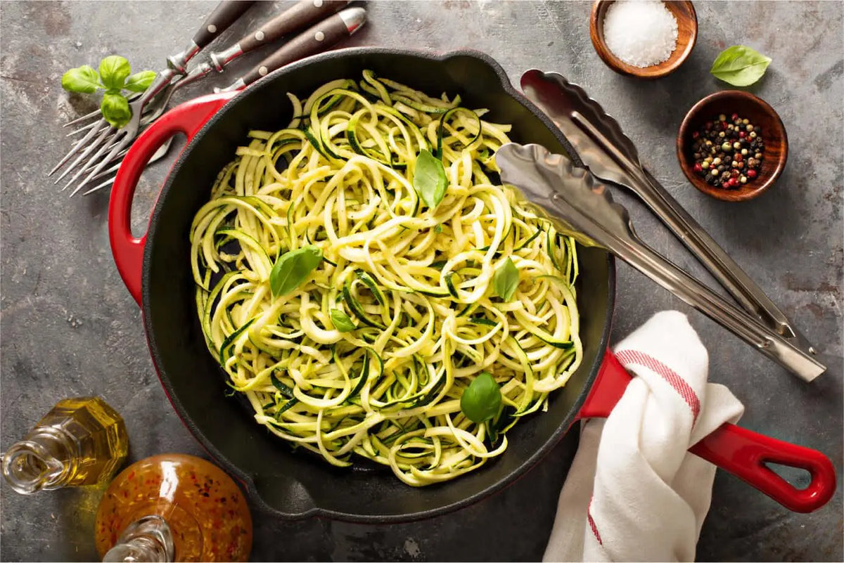 Macarrão de pupunha com pesto em frigideira vermelha, decorado com manjericão.