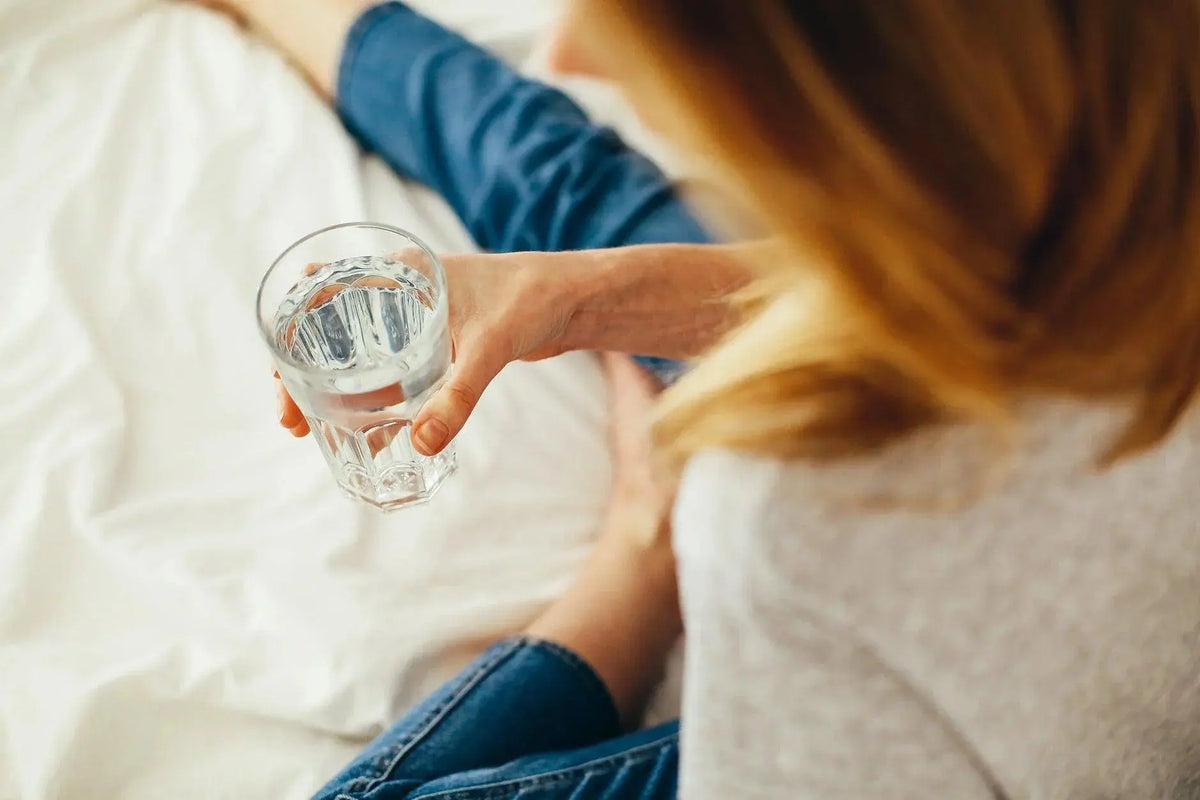 Texto alternativo:Mulher segurando um copo de água, simbolizando retenção de líquido.