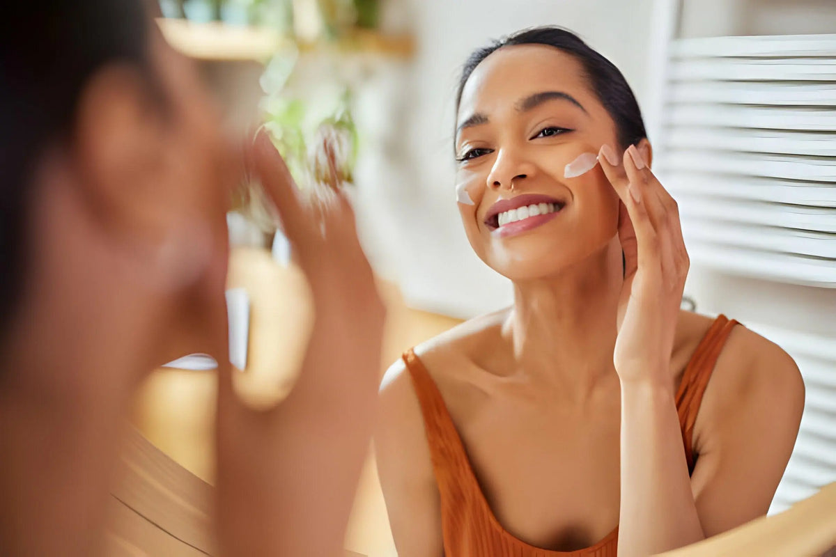 Mulher aplicando creme facial no espelho, cuidando da pele no verão.