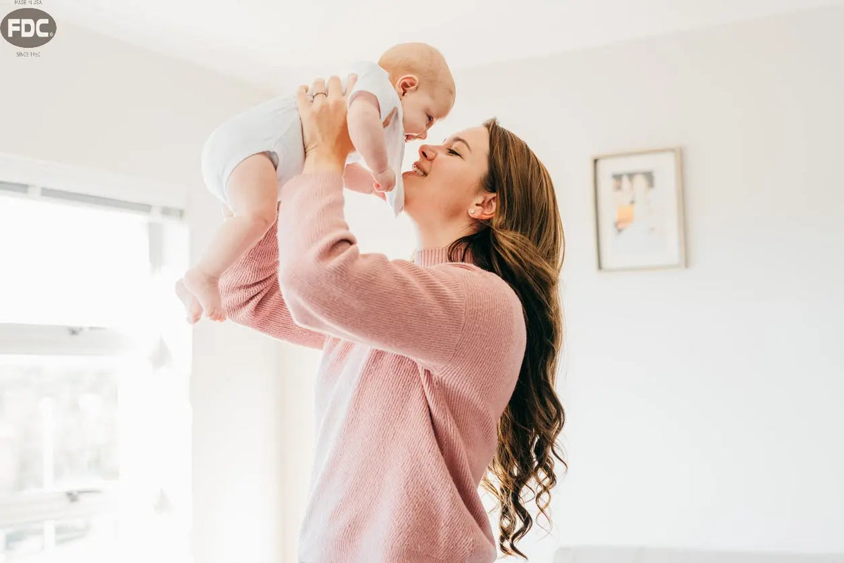 Texto alternativo:Mãe segurando e beijando seu bebê em um ambiente iluminado e acolhedor.