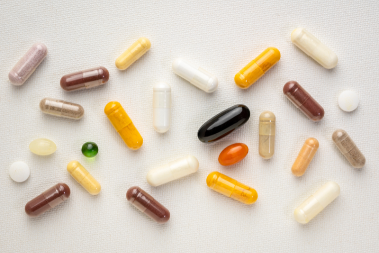 Diversas cápsulas e comprimidos de vitaminas em cores variadas sobre fundo claro.